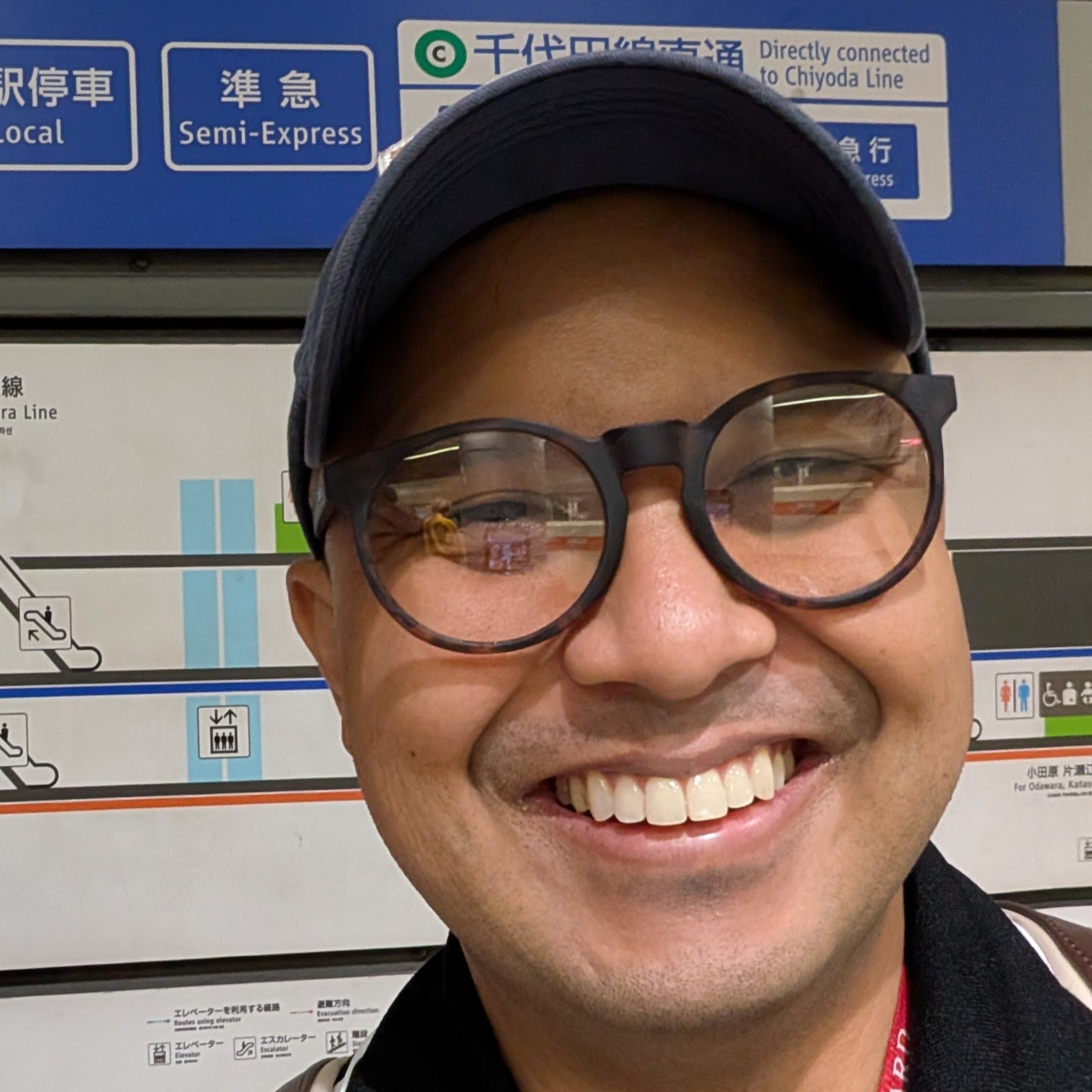 headshot of Oliver Mayor standing in front of a transit sign in Kanagawa, Japan